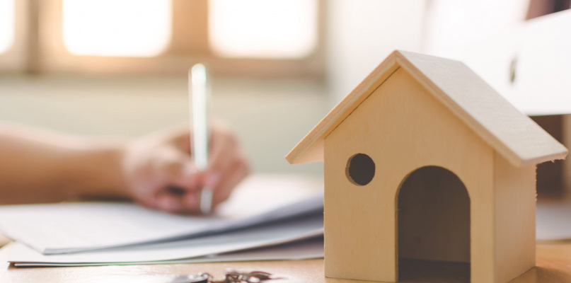 Wooden home model and key house on wood table with hand signing the document contract loan or mortgage property investment