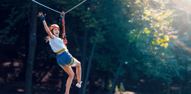 Happy women girl female gliding climbing in extreme road trolley zipline in forest on carabiner safety link on tree to tree top rope adventure park. Family weekend children kids activities concept