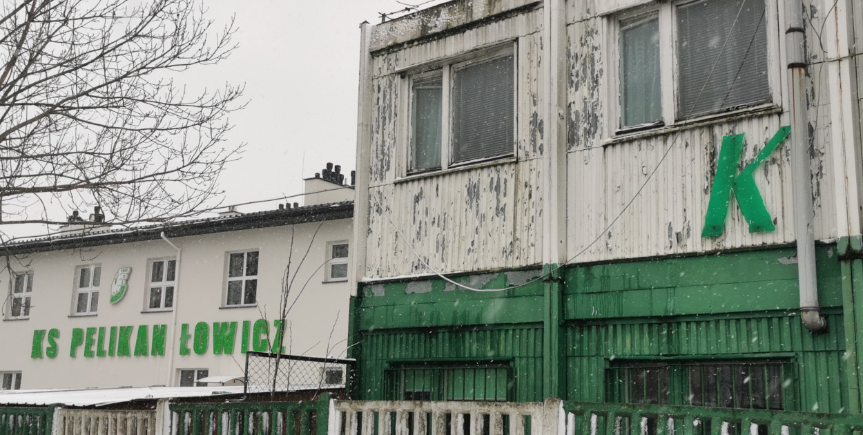 Szpetny stary budynek Pelikana, w tle nie użytkowany nowy. Za nimi kiepska  murawa stadionu, zbędna południowa trybuna, pod nią sterty śmieci. W rozliczeniach rosnące zaległości płatnicze. Sytuacja Pelikana u progu roku 2025 jest dramatyczna. 